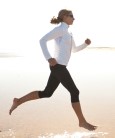 sporty woman jogging on wide sandy beach at bright sunshine